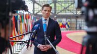 Puolustusministeri Antti Häkkänen haastattelussa, edessä ulkomaiden toimittajien mikrofoneja ja taustalla EU-maiden lippuja.