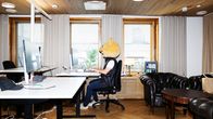 Henkilö istuu toimistotuolilla tietokoneen ääressä yllään toppaliivi ja nallen pää.