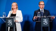 Riikka Purra ja Petteri Orpo seisovat puhujakorokkeilla sinisen taustan edessä, pöydillä lasilliset vettä ja mikrofoneja.