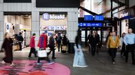 En grupp människor går genom en järnvägsstation med butiker i bakgrunden.
