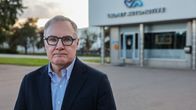 Vakavailmeinen, harmaahiuksinen mies tehtaan edustalla.