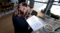 A person holds a floor plan drawing at an apartment viewing in a room with large windows.