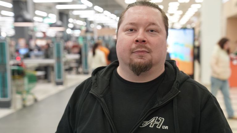 Mikko Perttola, asiakas jouluostoksilla seisoo kameraan katsoen kassajonon edessä Kaaren kauppakeskuksessa.