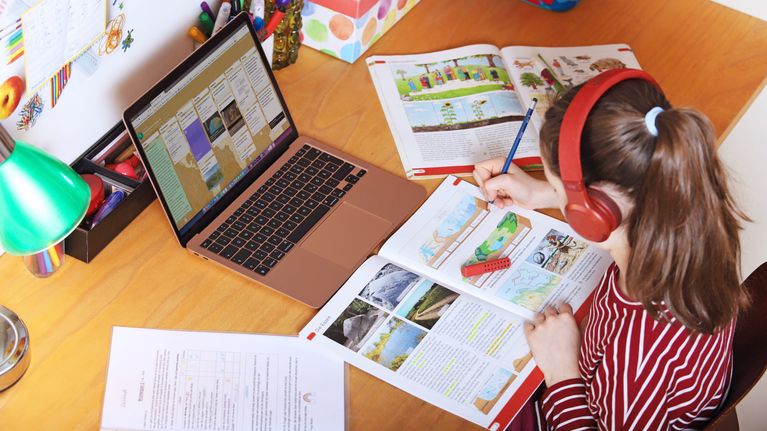 Girl sitting at a desk doing homework with books, notepads and a laptop computer on a desk.
