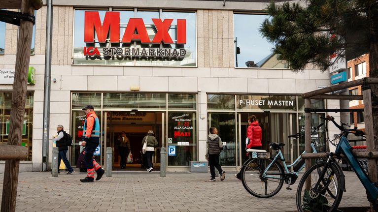 Useita ihmisiä kulkee sisään ja ulos Maxi Ica Stormarknad -ruokakaupan pääovista, edessä on polkupyöriä.