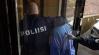 Poliisin virkailija saattaa sinitakkista henkilöä sisätiloihin osana virkatehtävää.