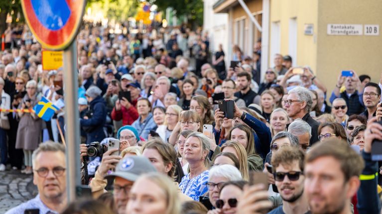 En folkmassa står på en gata med mobiltelefoner och kameror.