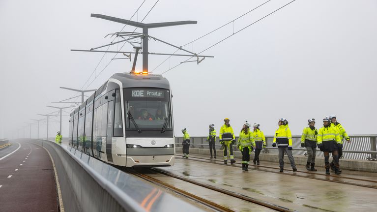 Raitiovaunu kulkee sillalla ympärillään huomiotakkeihin pukeutuneita rakennushenkilöitä.