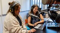 Kaksi henkilöä keskustelemassa podcast-studiossa mikrofonien ja kuulokkeiden ääressä.