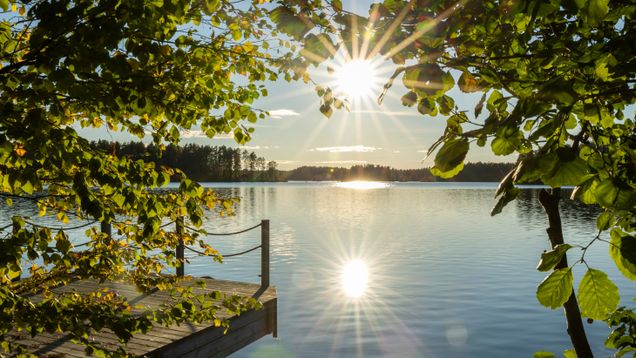 Kesäinen järvimaisema laiturilta katsottuna, auringonpaiste heijastuu veden pinnasta.