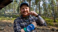 Mies metsässä esittelee kahta erilaista huivia, toinen kaulassa ja toinen ranteessa.