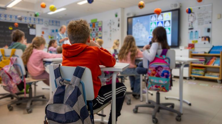 Children pictured from behind sitting in a classroom. 