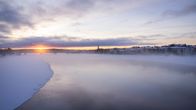 Kemijoki Rovaniemen keskustan kohdilla sulana, kaukaisuudessa auringonlasku.