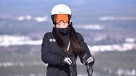 Lasketteluasuinen Anna Lukkari nojaa sauvoihin ja katsoo kameraan laskettelulasit silmillä.