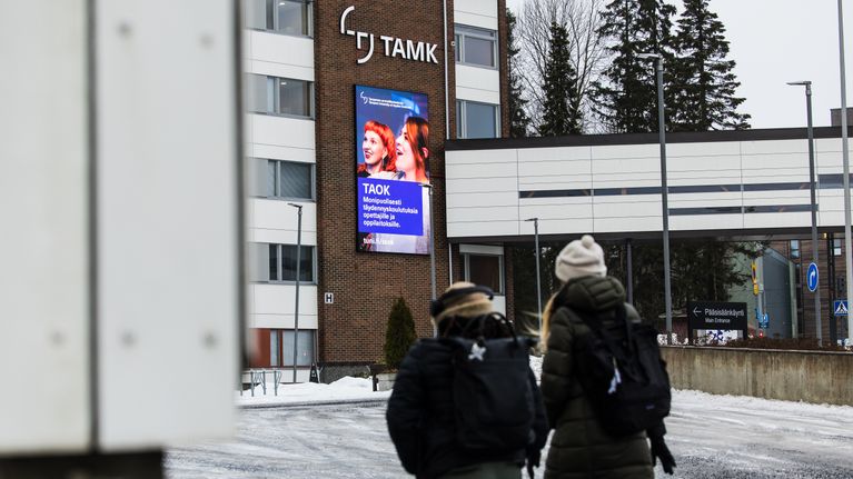 Kaksi henkilöä kävelee talvisäässä kohti Tampereen ammattikorkeakoulun tiilirakennusta.