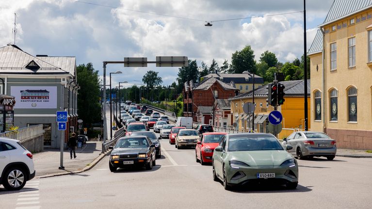 Busy car traffic on a street in a small city with old, low buildings and a cloudy sky.