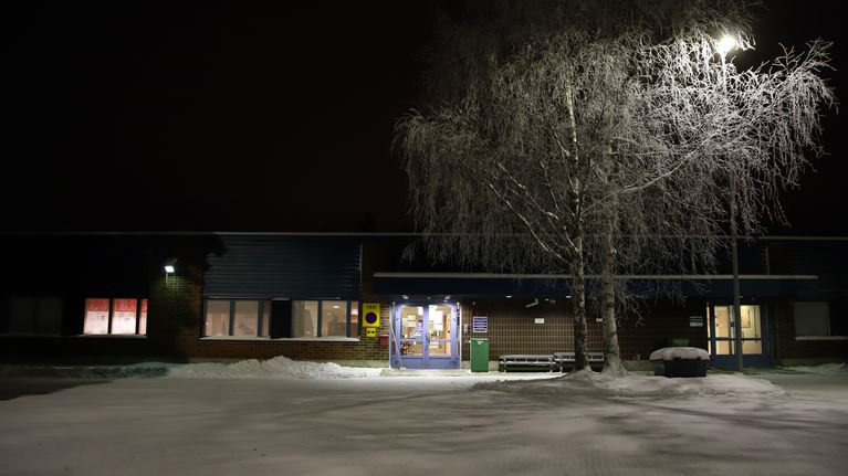 Punatiilisen matalan rakennuksen sisäänkäynti talvella katuvalon loisteessa.