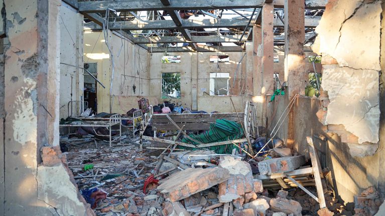 Ilmaiskussa vaurioitunut sairaalan huone, kattopalkkien välistä näkyy taivasta, tiiliä ja betoninkappaleita lattialla.