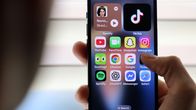 Photo shows a person holding a mobile phone with social media apps on the screen.