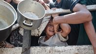 Palestiinalaiset jonottavat ruoka-apua kattiloiden kanssa. Aidan välistä näkyy itkevä lapsi.