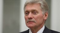 Dmitri Peskovilla on viikset, tumma puku, valkoinen kauluspaita ja kellervä kravatti.