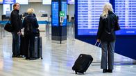 Three people with luggage and dark clothes standing in an airport terminal.