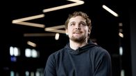 Huppariin pukeutunut Oliver Suvanto istuu kädet puuskassa ja hymyillen Tampereen areenan aulassa.