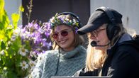 Två personer sitter utomhus vid ett bord med blommor, båda bär headset och har dator framför sig.
