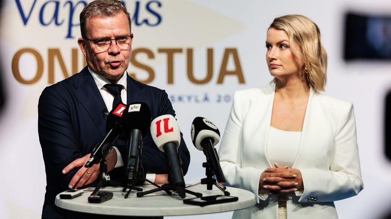 A man, Petteri Orpo, and a woman, Maggie Keskinen, stand at a podium.