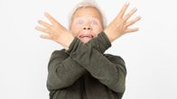 Nainen katsoo kohti ja pitää käsiään ristissä kasvojensa edustalla.