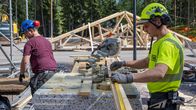 Two men working on a homebuilding site on a sunny summer day with trees in the background.