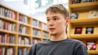 Mies istuu kirjastossa kirjojen ympäröimänä.