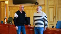 Två män står i ett rum inrett med träpaneler och tavlor på väggarna. Rummet är ett mötesrum.