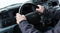 Henkilö istuu kuskin paikalla etupenkillä kädet Ford-merkkisen auton rattia pidellen.