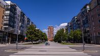 A view down a long street lined with trees and apartment buildings. There is a Wolt courier on a bicycle in the distance.