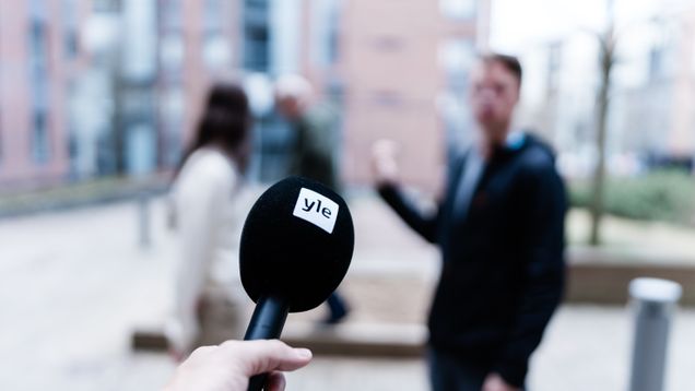 Ylen mikroni osoittaa kohti kahta haastaltavaa, miestä ja naista.