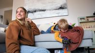 Nainen ja pieni lapsi leikkivät olohuoneessa. Nainen istuu lattialla, pieni lapsi makoilee sohvalla.