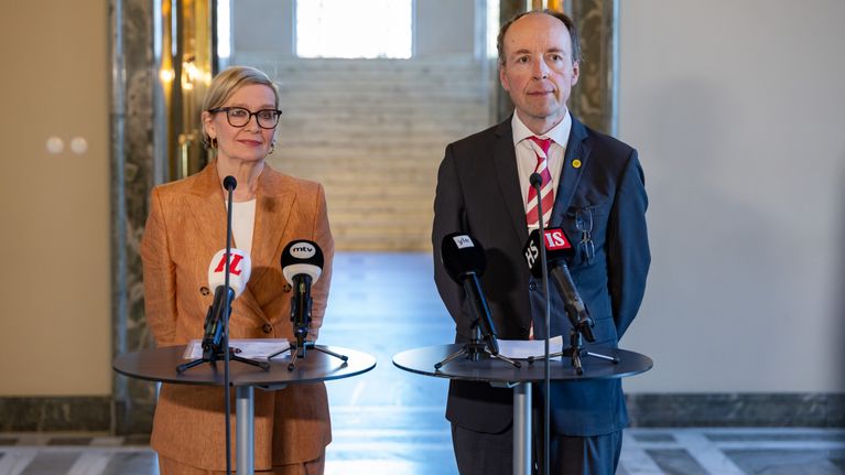 Paula Risikko and Jussi Halla-aho standing in front of a microphone, talking at a press conference.