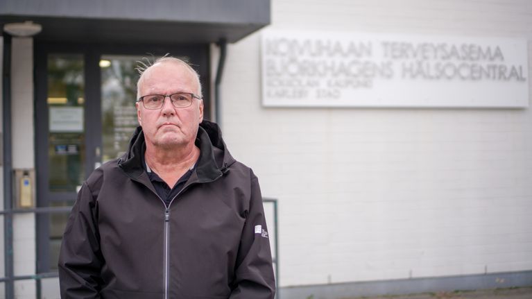 En person står framför en byggnad med en skylt där det står "Björkhagens hälsocentral".