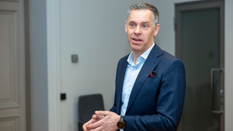 En man i blå kostym gestikulerar med händerna medan han berättar om ekonomi. 