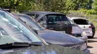 Rivissä useita henkilöautoja pysäköitynä ulkona, taustalla puita ja metallinen aita.