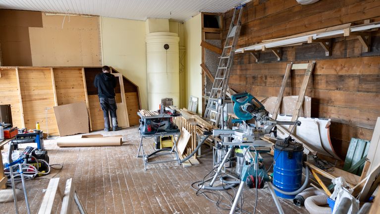 En person arbetar i ett rum under renovering med verktyg och byggmaterial utspridda på golvet.