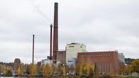 Suuri tehdasrakennus syksyisessä maisemassa. Rakennusta hallitsee valtavan korkea punatiilinen piippu.