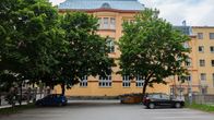 Kaksi henkilöautoa pysäköitynä parkkipaikalle suuren koulurakennuksen eteen.