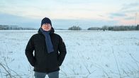 En person står på ett snötäckt fält, klädd i vinterjacka, mössa och halsduk.