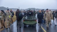 Ihmisiä telaketjuilla kulkevan droonin vieressä.