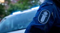 En anonym polis som bär polisens symbol på armen. I bakgrunden skymtar en polisbil.
