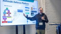 Kuvassa henkilö esittelee Riihimäki Defence Platform -kokonaisuutta. Näytöllä näkyy kartta ja lista yrityksiä, kuten Millog, Sako ja Hyria, sekä startup-yrityksiä, kuten VARS, Verdante ja TeppoTech.