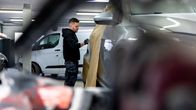 Mies mustassa hupparissa hiomassa maalattavaa autoa.