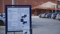 Kuvassa näkyy monitoimitalon piha-alueen kartta ja taustalla parkkipaikalla on autoja.